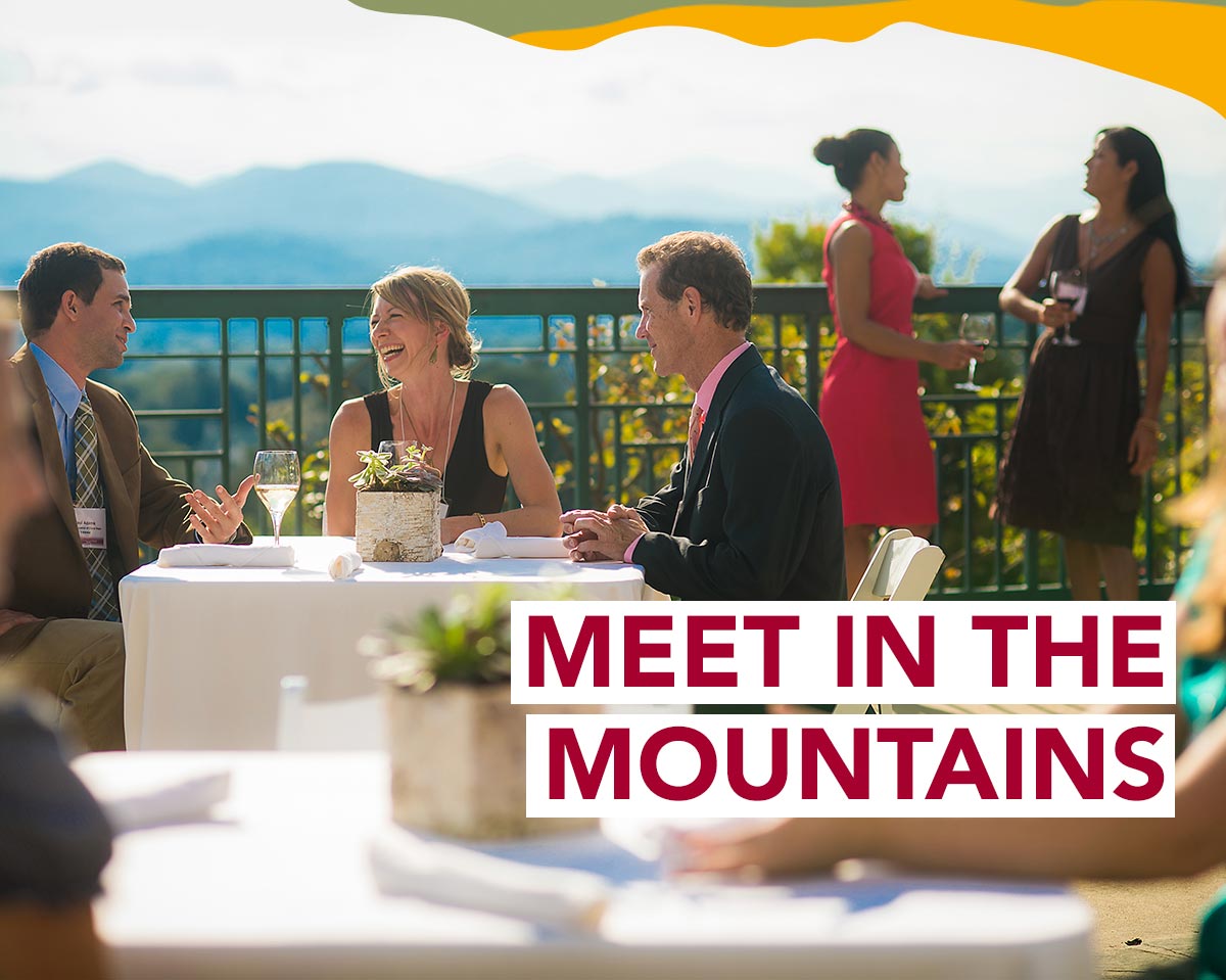 Colleagues having drinks on a restaurant terrace with mountains in the distance. A headline reads: Meet in the Mountains.