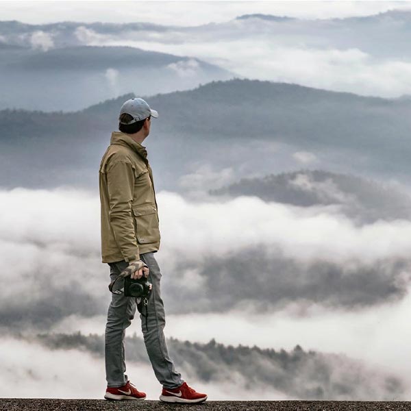 A photographer looking at a scenic view of clouds and mist rising up between a series of mountainous hills.