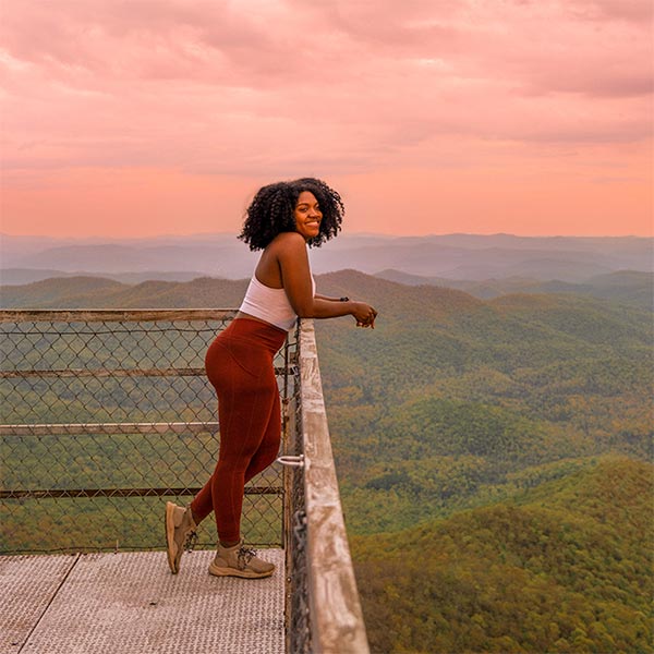 A woman on an overlook admiring beautiful landscape among a red-colored sunrise.