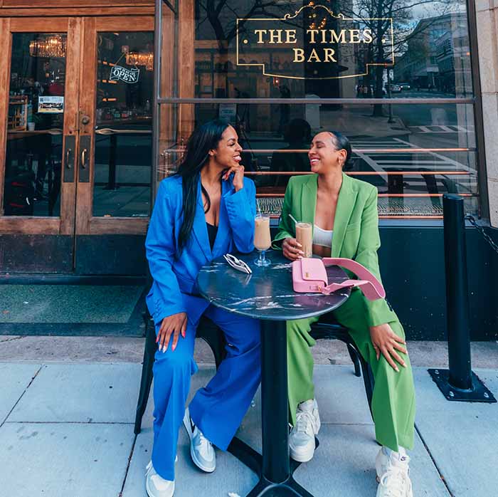 Two women sitting outside of a bar with drinks.