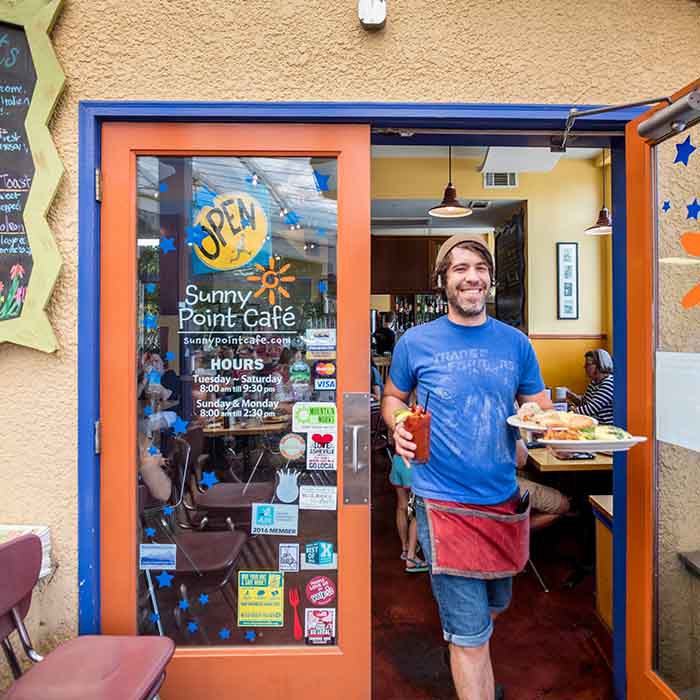 A man walking out of a restaurant holding a drink and food.