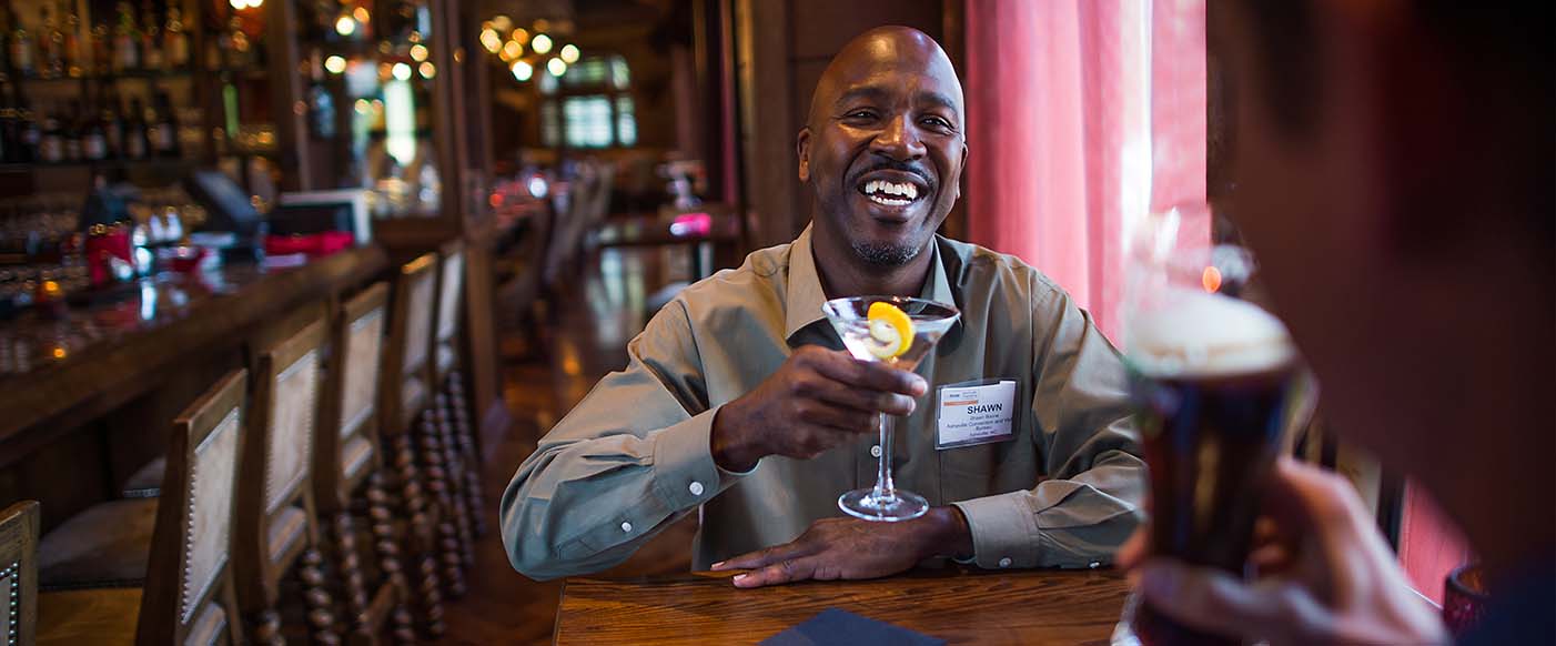 A man holding up a drink at a bar.