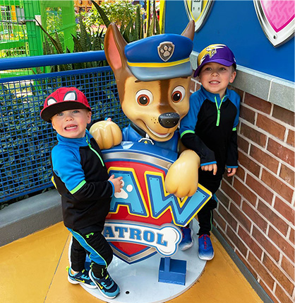 A photo of two young boys posing with a Paw Patrol statue. 