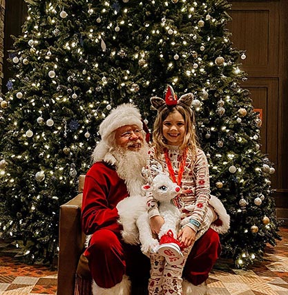 A photo of a young girl on Santa's lap in front of a Christmas tree.