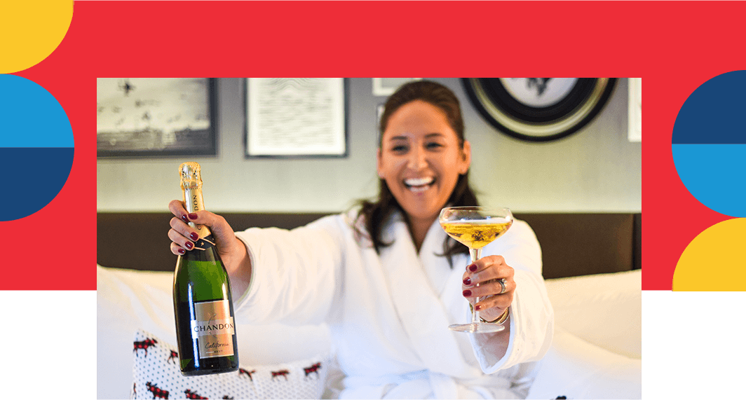 Smiling woman wearing robe in hotel room holding champagne.