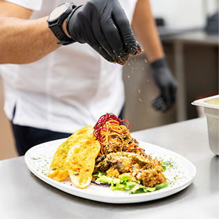 A man sprinkling a topping onto a food dish.