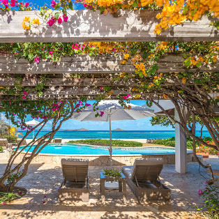 An outdoor table, beneath a pergola, with a view of the sea.