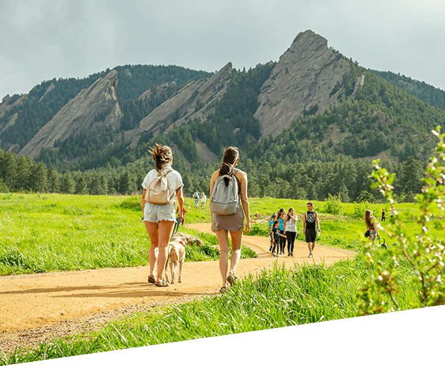 Girls and dog hiking on a path with mountains in the background.