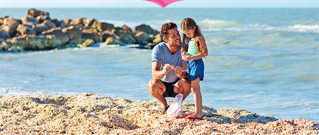 Picture of father and daughter on the beach looking at a shell. 