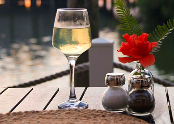 A glass of wine on a table next to the ocean. 
