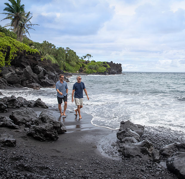 Two men walk on a black-sand beach