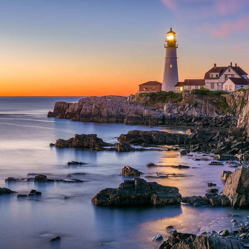 Lighthouse on cliff with the sun setting over the ocean. Click here to book.