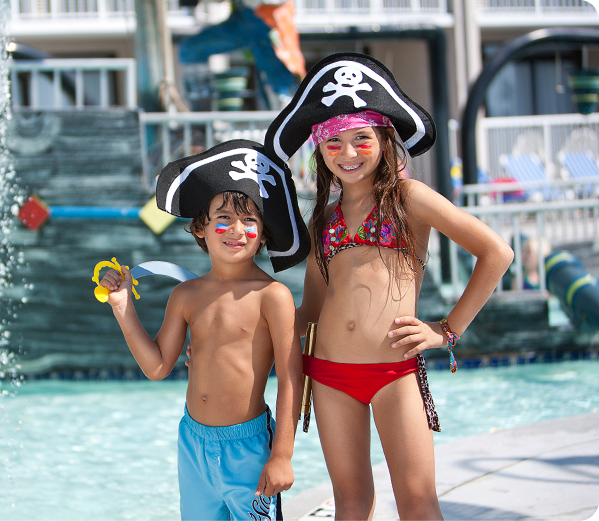 A brother and sister wearing swimsuits and pirate hats.