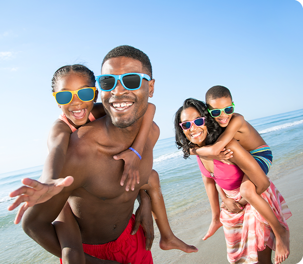 A father and mother giving their kids piggy-back rides on the beach.